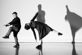 A black and white photo of 2 dancers with their silhouettes behind them.